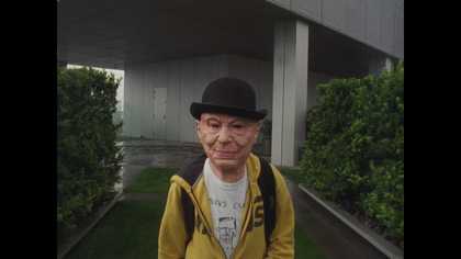a person in an old man mask looking into the camera