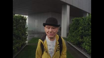 a person in an old man mask looking into the camera