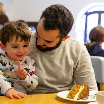 a parent and child sat at a table with a slice of cake and a coffee.