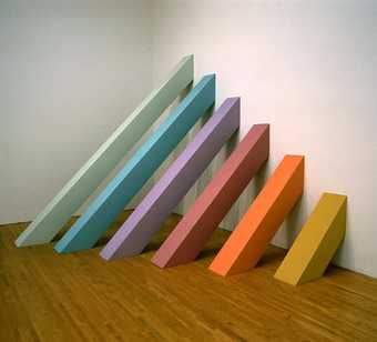 Fig.12 Sculpture by Judy Chicago installed in a gallery featuring 6 square planks running from floor to wall; each is painted a different colour and the length varies by increments, with the shortest nearest the camera