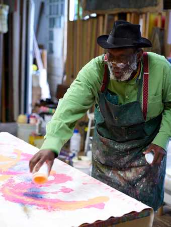 Fig.13 Frank Bowling pouring acrylic paint onto the canvas, having mixed it with ammonia in an old paint pot prior to application Photo: Jäger Arén