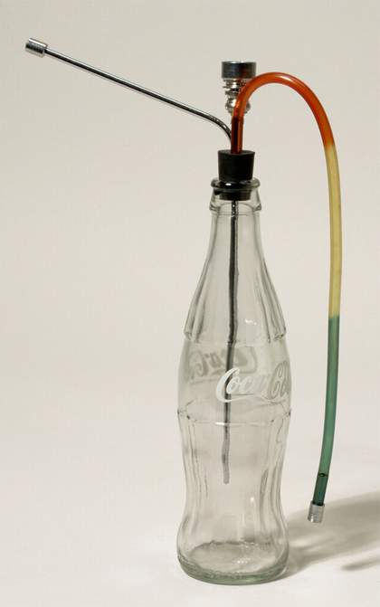 An empty, clean Coca-Cola bottle with a pipe attachment placed in its mouth.
