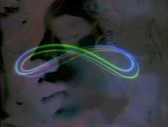 Video still showing a dark background of feint, abstract forms overlaid with bright, glowing, coloured lines in an infinity shape