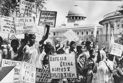 A large crowd of figures march and hold up banners in an outdoor setting.