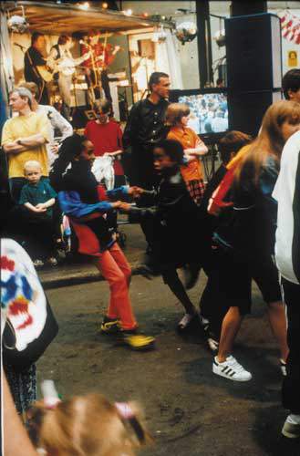 Young people dance in an outdoor setting, with a band playing in the background