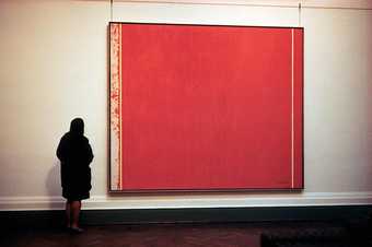 Photograph of a large red abstract painting by Barnett Newman hanging on a gallery wall with a person standing looking at it