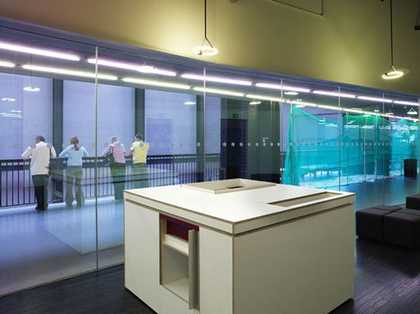 A cube resembling functional gallery furniture installed at Tate Modern; there are openings like display spaces visible on the top and sides of the cube