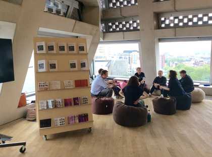 A group of people sitting on beanbags and talking next to a bookshelf.