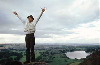 Photograph of Joseph Beuys standing on the peak of a hill with the valley below, his arms reaching to the sky