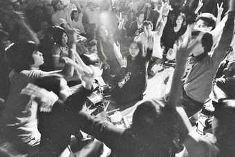 Black-and-white photograph of people kneeling on the floor holding one arm in the air and making the peace sign with two fingers