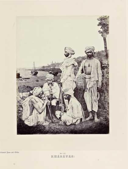 A group of figures, some standing and some sitting, in an outdoor setting with a shore and boats in the background.