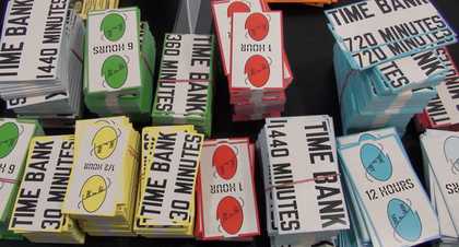 Stacks of coloured pieces of paper with 'Time Bank' and different numbers of minutes and hours written on them.
