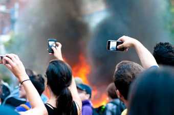 ‘A crowd of spectators using their mobile phones to capture footage of a burning police car on Queen St. W. in Toronto during the 2010 G20.’