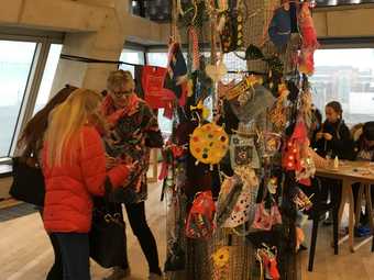 People stand and talk next to a fabric installation that hangs from the ceiling and has multicoloured pieces of textile attached to it.