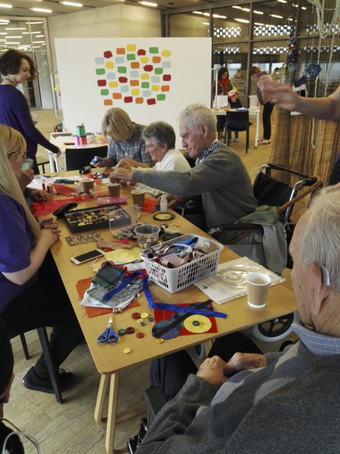 A group of older people sit working around a table that is covered with craft materials.