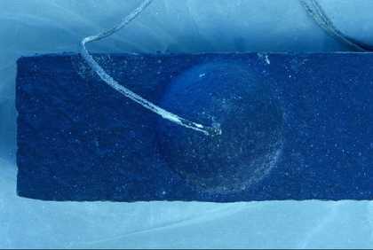 A close-up from above of one of the hemispheres in Addendum, showing lighter tones on the rope that emerges from it and lighter-toned spots and dribbles on the wood and papier mâché structure that supports it.