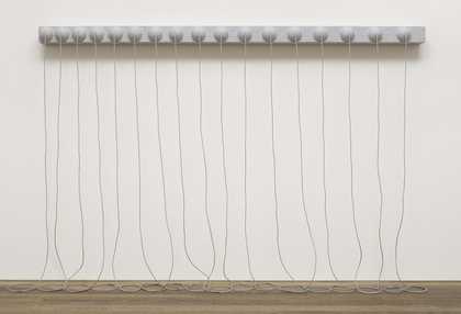 A grey sculpture consisting of a narrow, horizontal panel with seventeen hemispheres on its face, fixed to the wall around two metres above the floor, with long ropes from the centre of each hemisphere that hang down and rest in coils on the floor