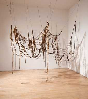 A large sculpture consisting of brown lengths of string, wire and rope that hang from the ceiling in a drooping network of loops, occasionally touching the floor.