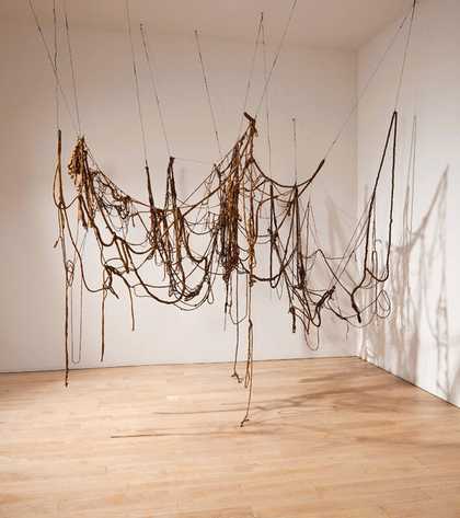 A large sculpture consisting of brown lengths of string, wire and rope that hang from the ceiling in a drooping network of loops, occasionally touching the floor.
