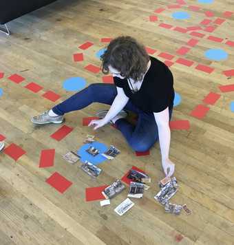 A person sits on the floor arranging pieces of coloured paper and photographs.