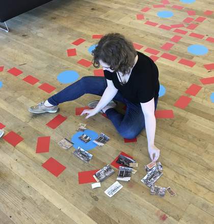 A person sits on the floor arranging pieces of coloured paper and photographs.