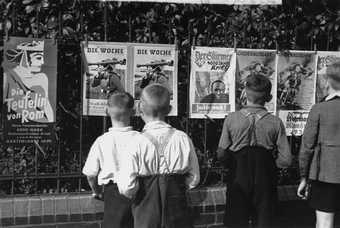 Julien Bryan, A group of young German boys view Der Stuermer, Die Woche and other propaganda posters that are posted on a fence in Berlin, 1937