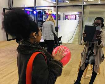 A person holds a balloon while another person photographs them using a tablet computer.