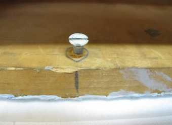A close-up view showing a nail emerging from a piece of wood, with a circular pencil line surrounding it and a vertical line drawn above it.