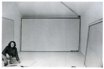 Bob law photographed crouching in a gallery space in front of a large canvas with a black rectangle drawn around the edge.