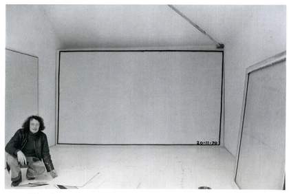 Bob law photographed crouching in a gallery space in front of a large canvas with a black rectangle drawn around the edge.