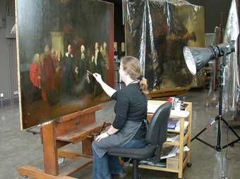 A person sitting in front of a painting and gently removing the varnish with a cotton bud