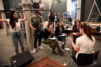 A person speaks and gestures with their hands while being interviewed for a film - there is a panel of three people behind the camera as well as a camera operator and a boom operator