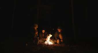 Three young people around a bonfire