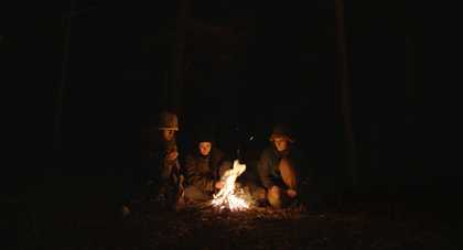 Three young people around a bonfire