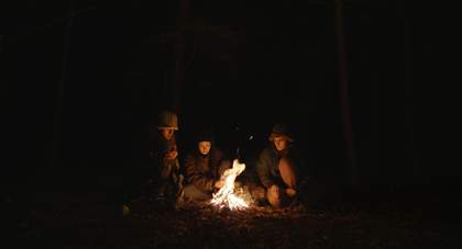 Three young people around a bonfire
