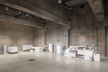 a large white room with wooden floors and large rectangle windows in the ceiling is filled with plinths, pallets, and various DIY materials.