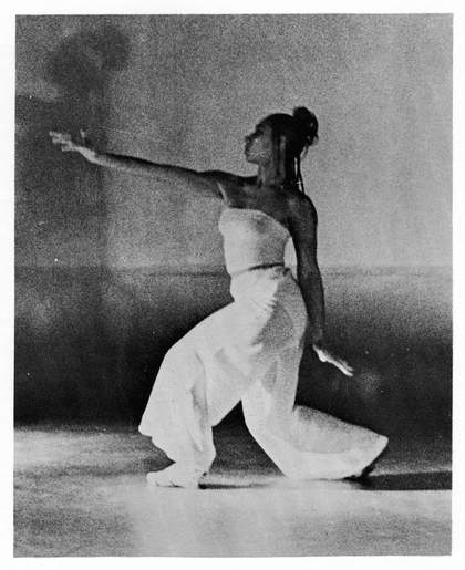 black and white still from a film, one woman poses with arm in the air 