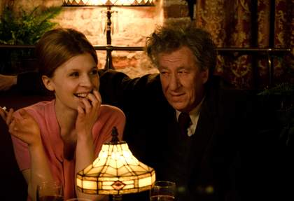 a film still from Final Portrait showing a woman and man sitting at a table 