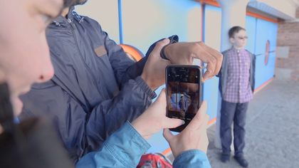 a man uses his hand to make a circle, through which a woman points her camera phone at a boy