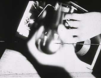 Hands are seen touching a small device in this black and white image