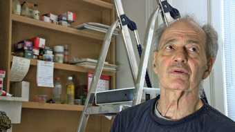 Film still of Frank Auerbach in his studeio with paint pots and a ladder behind him