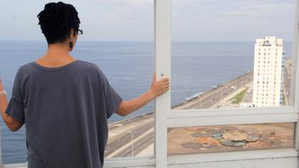 film still of a woman looking out of glass window to the sea