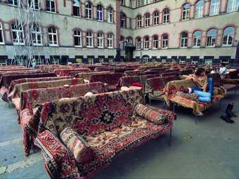 Series of sofas covered by patterned rugs and arranged in rows in a courtyard