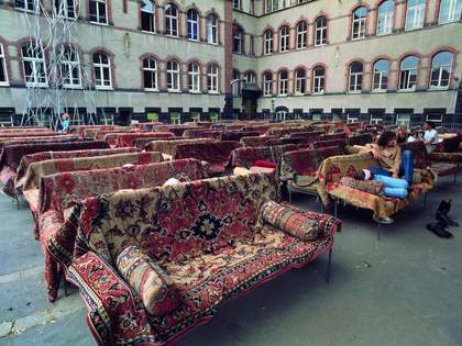 Series of sofas covered by patterned rugs and arranged in rows in a courtyard