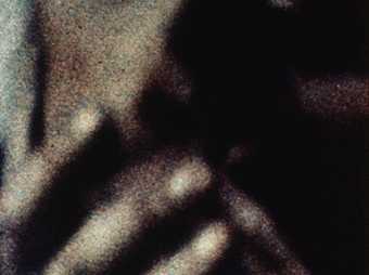 Grainy close up of a black and white image of a person holding their hands up to their face