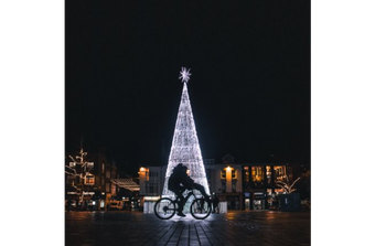  Two people ride on a bike in front of a lit christmas tree 