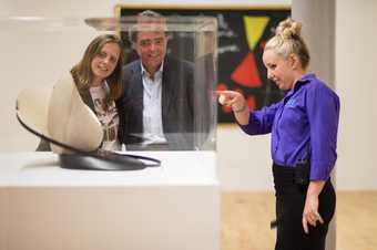 Two visitors in Tate Liverpool gallery look at a sculptural art piece and talk to a Tate visitor assistant