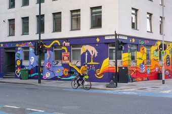 A person cycles past a mural covering two sides of a building