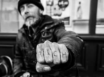  A man holding out a fist. The word rich is tattooed on his knuckles 