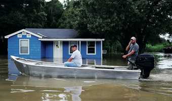 People drive through a flooded road by boat as they visit their neighbourhood on 16 August 2016 in Sorrento, Louisiana